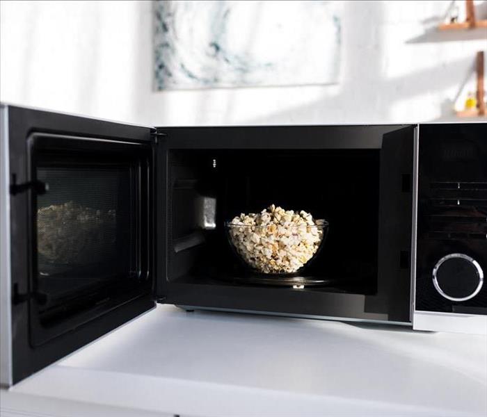 Image of a microwave with a bowl of pop corn inside. 
