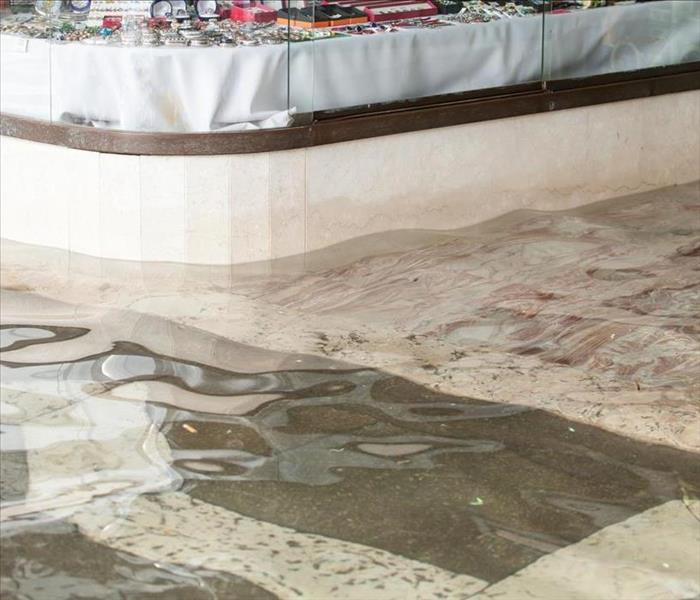 Image of a flooded street with water entering in a local store. 